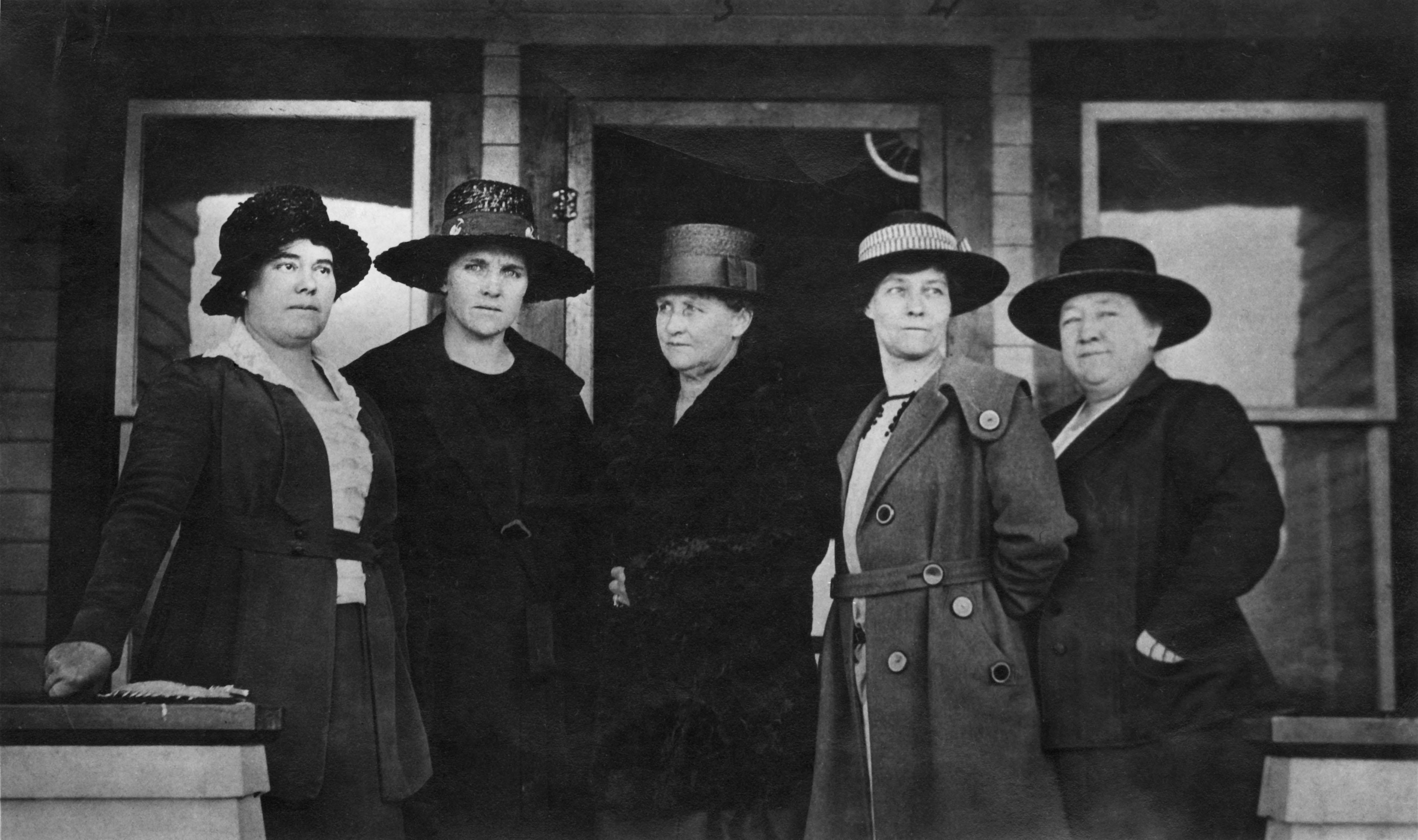 black and white photograph of five women standing in a row in front of a building